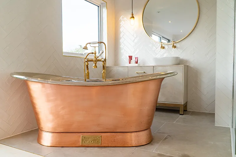 Copper roll-top bath beneath a round brass mirror